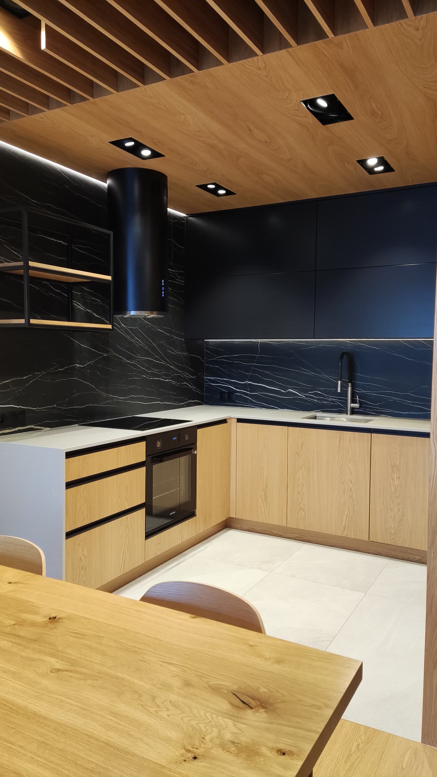 Czarna kuchnia z dekorem kamienia i jasnym drewnem w nowym mieszkaniu